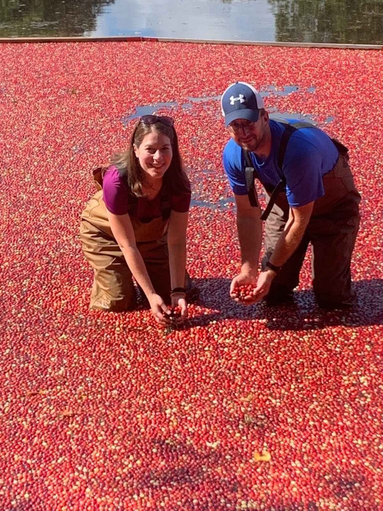 A woman and man on a Family Cranberry Bog Tour in waders surrounded by floating cranberries.