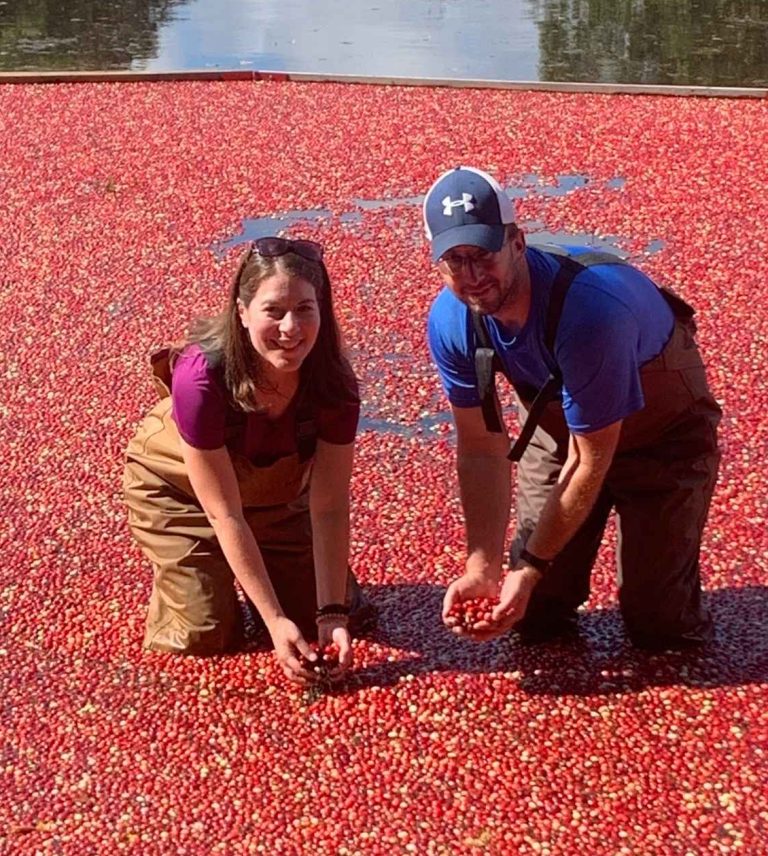 A woman and man on a Family Cranberry Bog Tour in waders surrounded by floating cranberries.