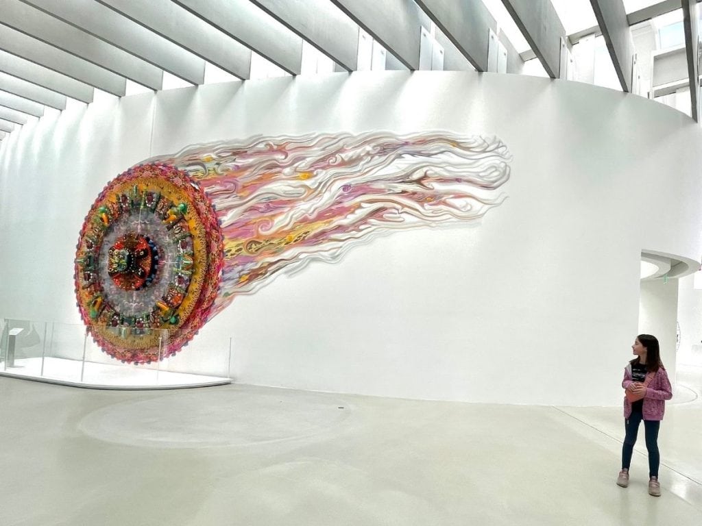 Is Corning Museum of Glass good for kids? A young girl stands in awe of a colorful fireball sculpture on a white museum wall.