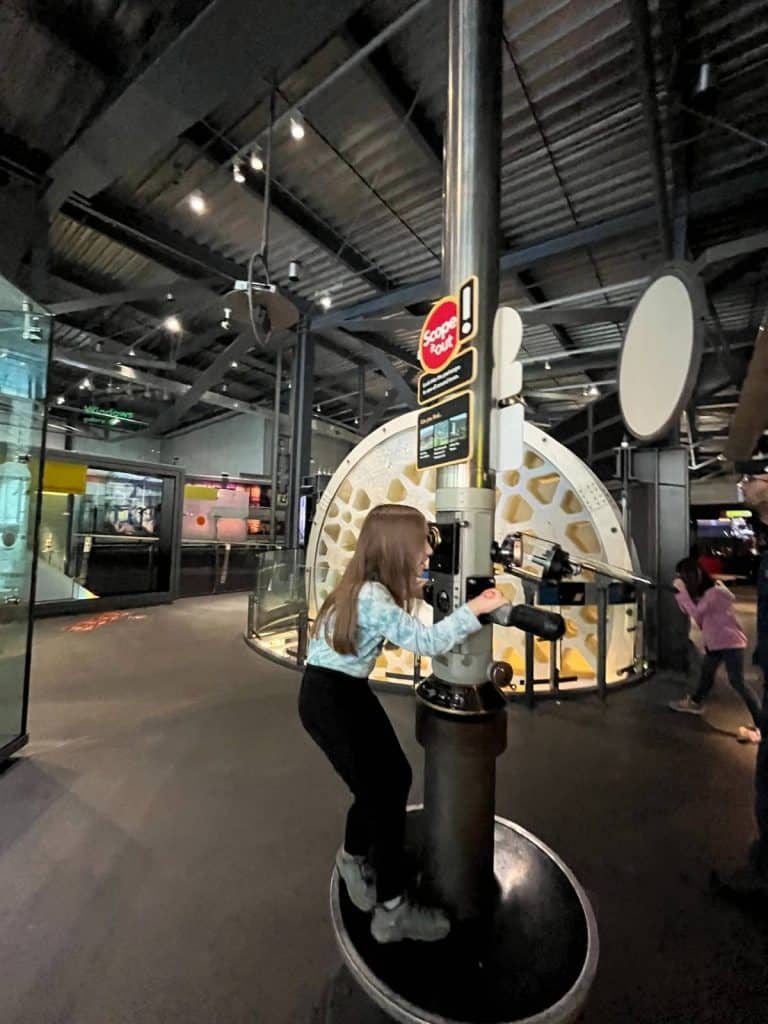 A child interacts with a large periscope exhibit in the Innovation Center, helping to answer yes to the question Is Corning Museum of Glass good for kids?