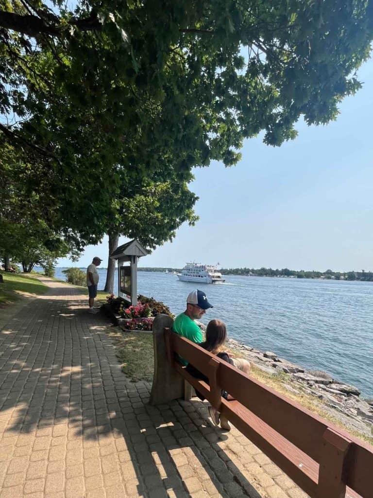 Dad and daughter sitting on a bench watching boats on the St. Lawrence River