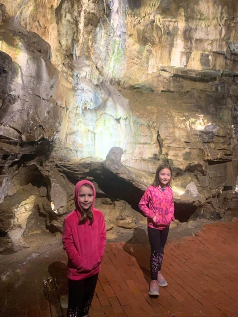 A picture of two girls smiling in pink sweatshirts on a lit path in an underground cave in New York.