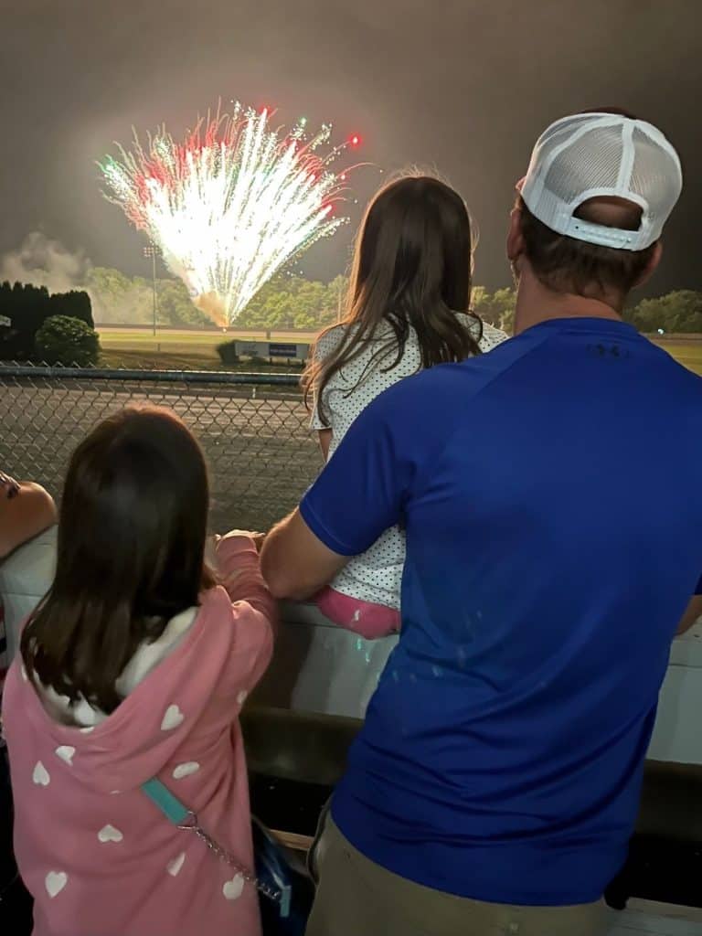 Showing our family at a local event. A dad and two girls watching fireworks at a Tioga Downs harness racing racetrack in New York.