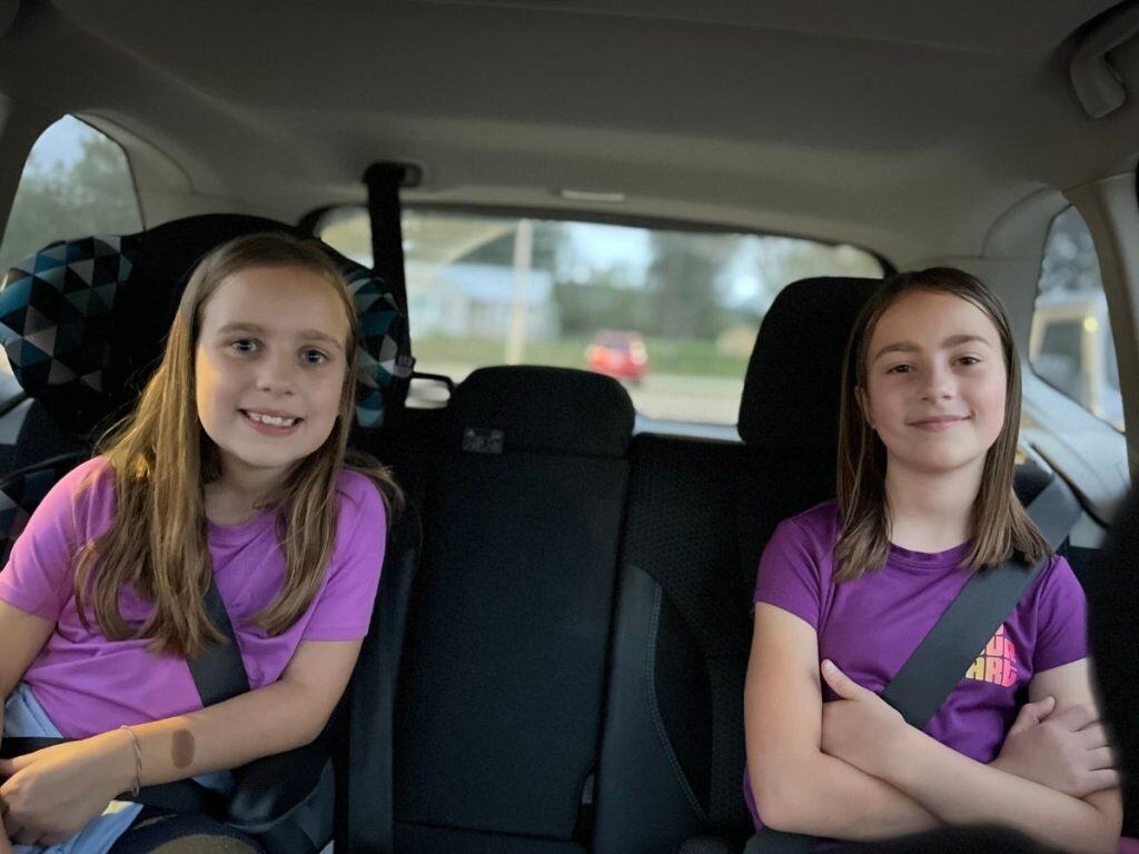 Our family takes a lot of road trips. Two girls in purple in a car backseat on a day trip.